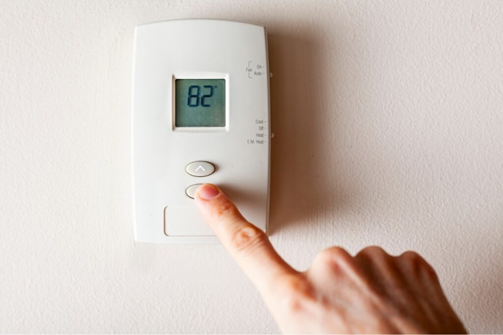 Person adjusting a thermostat set to 82 degrees Fahrenheit.